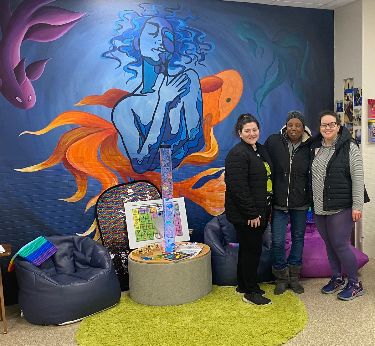 three people standing in front of a colorful mural in a sensory room.